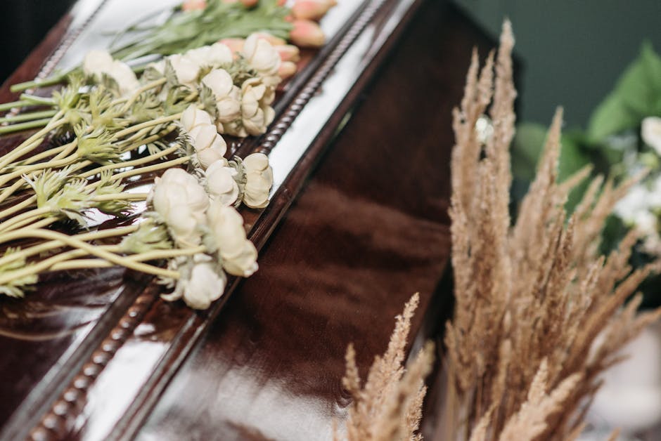 A close-up of a floral arrangement on a polished dark wooden surface, featuring a row of white, cream, and pale peach roses laid out with their stems extending along the surface, complemented by soft
