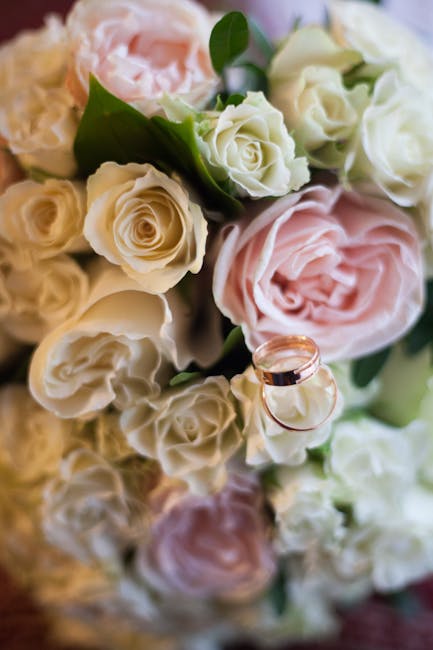 A close-up of a floral arrangement featuring a bouquet of soft pink and creamy white roses, with some pale green leaves interspersed among the blossoms. The roses are in full bloom, with delicately la